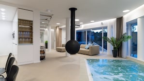 A modern interior with a glass staircase, a large black spherical object, a beige sofa, a small pool, and a potted plant.