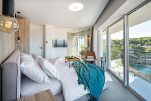 Een moderne hotelkamer met een groot bed, een klein tafeltje, een stoel en een balkon met uitzicht op zee.