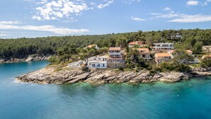 A coastal property with multiple buildings, rocky terrain, and a clear blue sea.