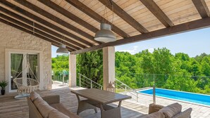 A covered outdoor area with wicker furniture, a pool, and a view of lush greenery. - Villa Belle with Pool (Vižinada)
