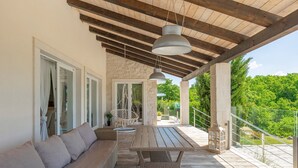 A covered outdoor seating area with a sofa and a table, a hanging light fixture, and a view of greenery. - Villa Belle with Pool (Vižinada)