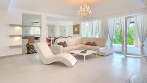 A modern living room with a white sofa, a glass coffee table, and a chandelier. - Villa Belle with Pool (Vižinada)
