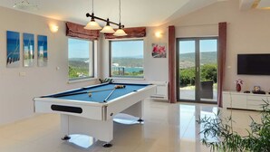 Een moderne kamer met een pooltafel, grote ramen met een panoramisch uitzicht en een flatscreen televisie.