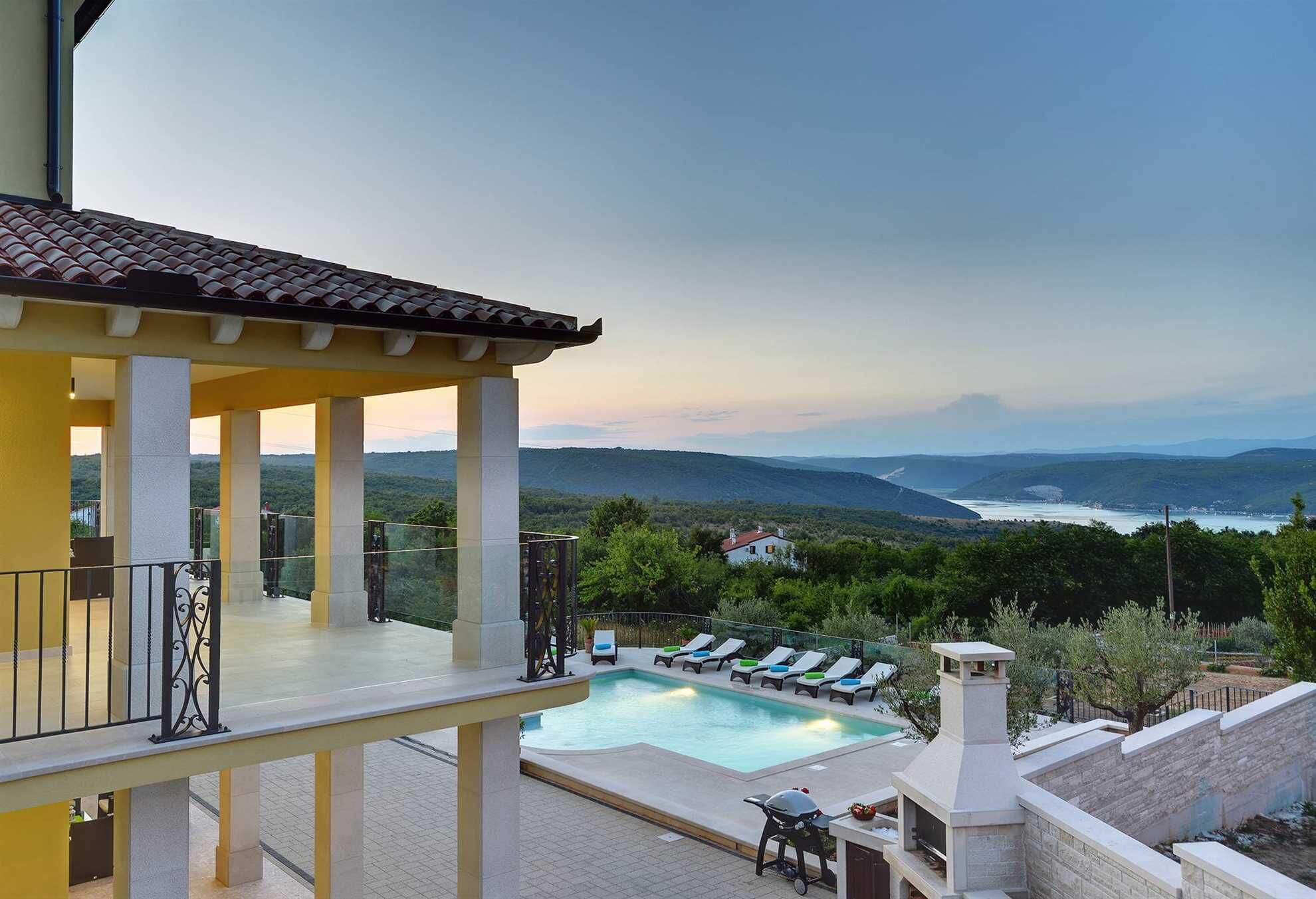 A pool area with lounge chairs, a barbecue, and a view of the landscape.