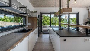 A modern kitchen with a central island, built-in appliances, and large windows offering a view of greenery.