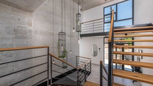 A modern interior with a concrete wall, a staircase with wooden railings, and hanging light fixtures.