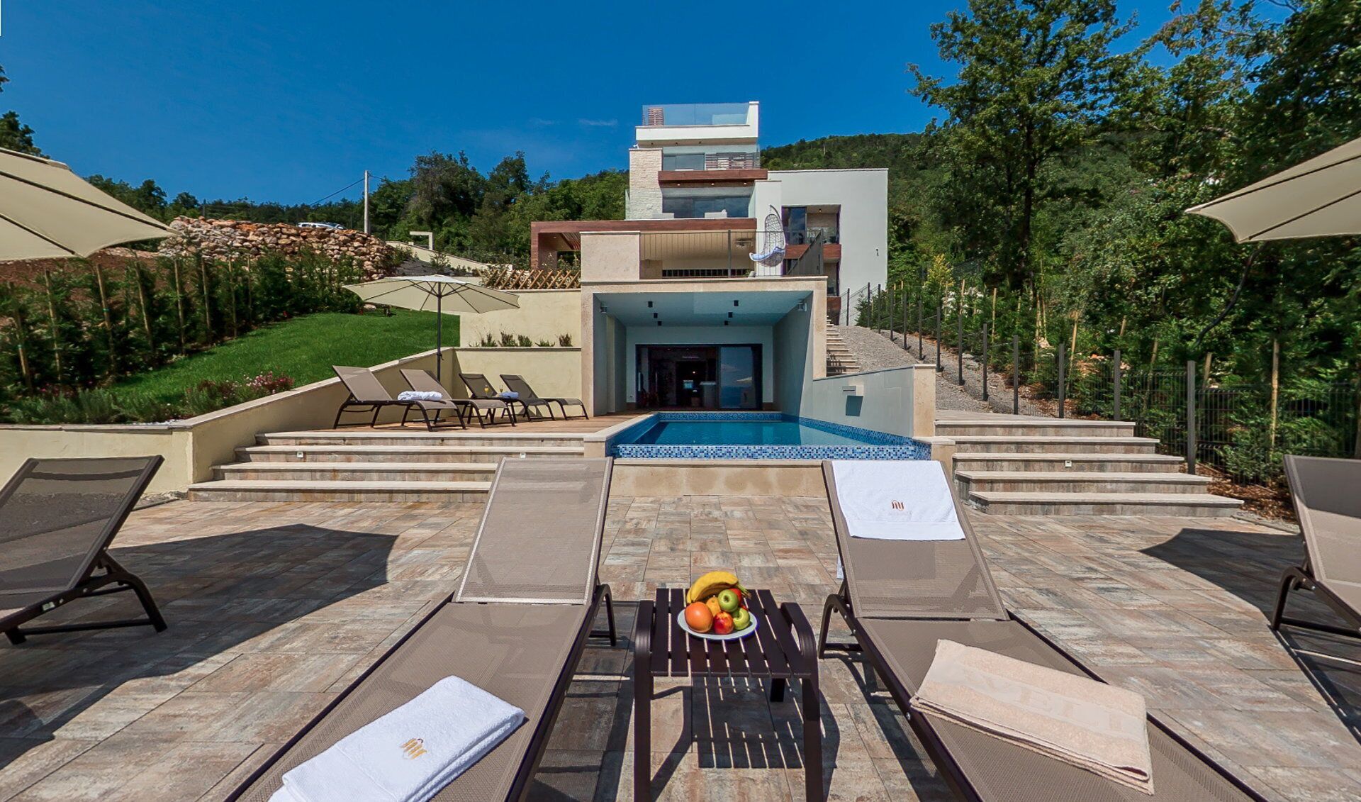 A modern villa with a swimming pool, outdoor seating, and a staircase leading to the entrance.