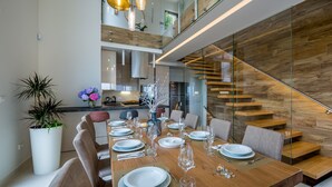 Un espace de salle à manger moderne, avec une table en bois dressée pour six personnes, entourée de murs en verre et d’un escalier en bois.