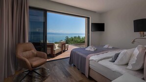 Une chambre d’hôtel avec un lit, une chaise, une télévision et une grande fenêtre donnant sur la mer.