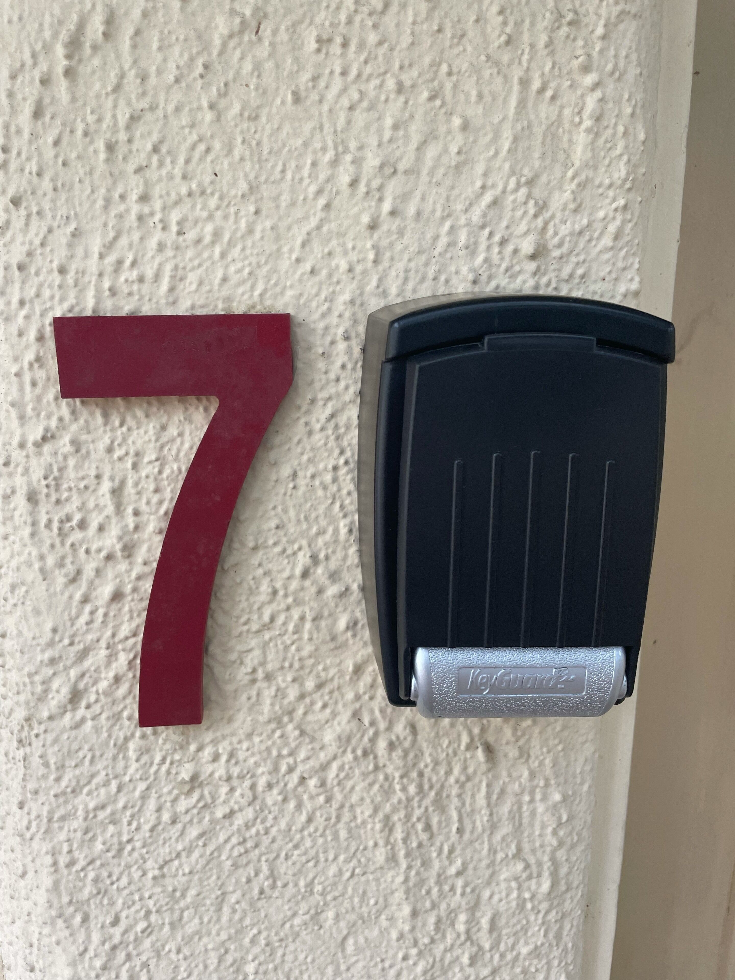 Eine rote Sieben auf einer strukturierten Wand, neben einem schwarzen Gegensprechanlage.