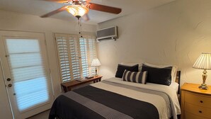 Et soveværelse med seng, to sengeborde, ventilator i loftet og et vindue med persienner.