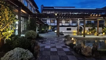 Un patio tradicional al estilo japonés con un sendero de piedra a cuadros, un estanque de carpas y un corredor cubierto.