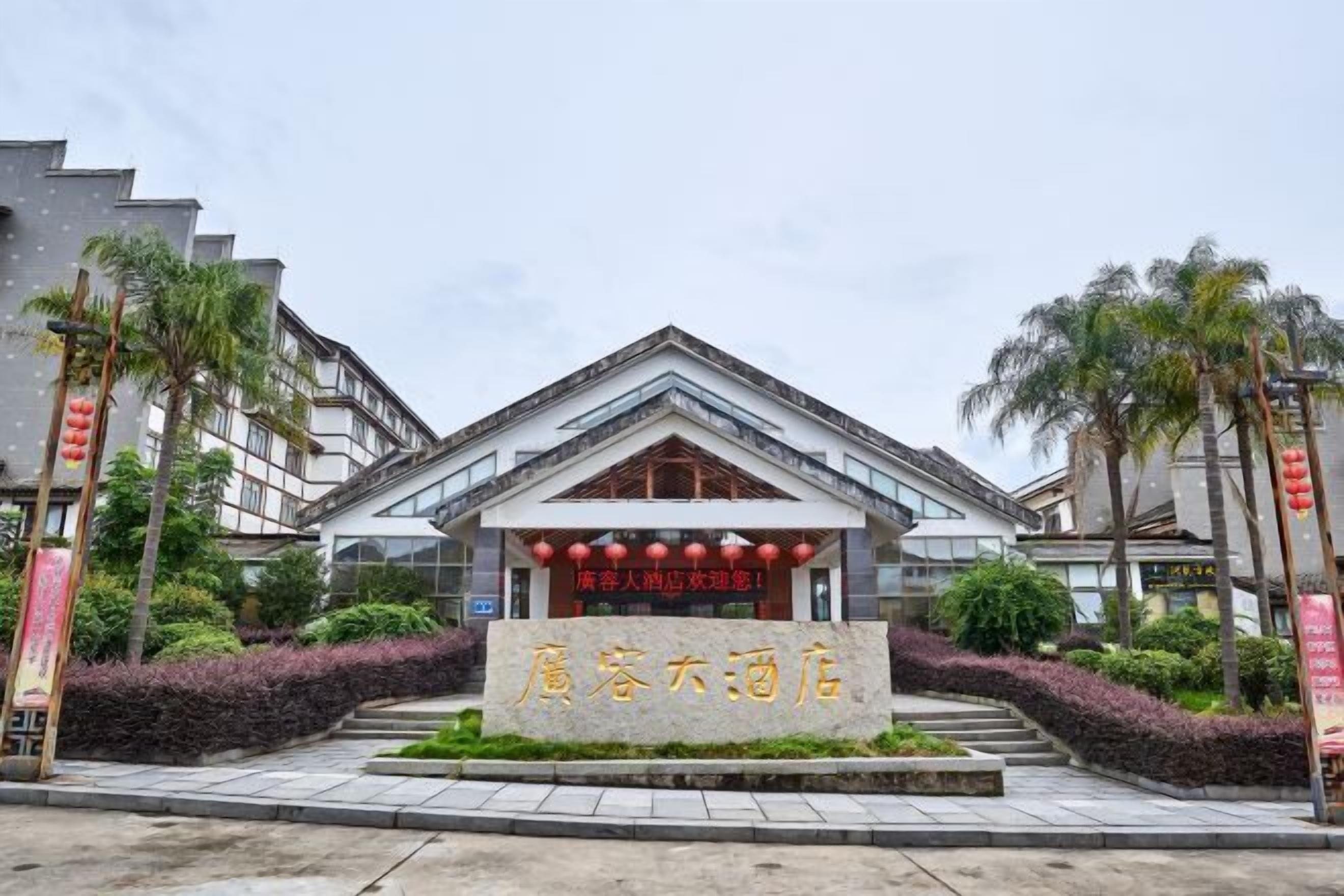 A hotel entrance with a stone sign, modern architecture, and surrounding greenery.