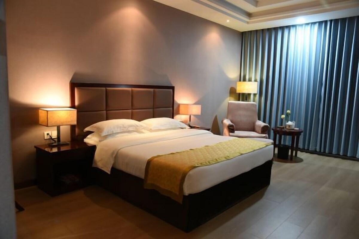 A hotel room with a large bed, two bedside tables with lamps, a chair, and a view of the city through curtains.
