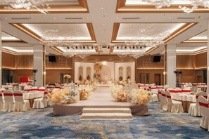 A banquet hall with round tables, a central aisle, and floral arrangements.