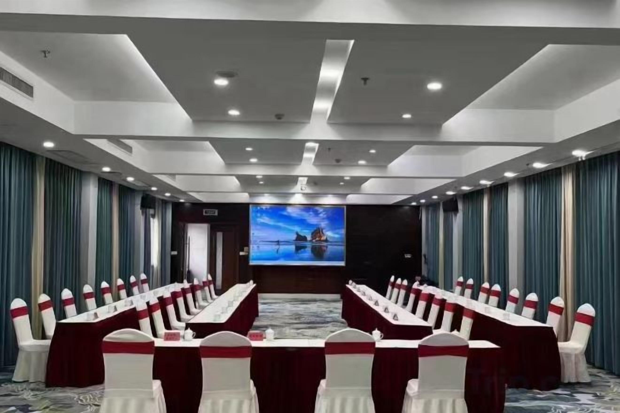 A conference room with a long table, chairs, a screen, and curtains.