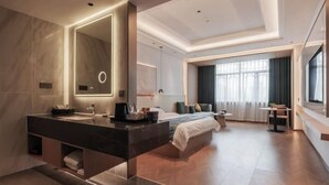 A modern hotel room with a large bed, a separate sitting area, a large mirror, and a bathroom with a double sink. - Guangrong Hotel (Sanming)