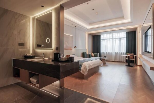 A modern hotel room with a large bed, a separate sitting area, a large mirror, and a bathroom with a double sink.