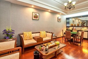 Una sala acogedora con sofá, mesa de centro y sillones. Se observa una mesa de comedor con sillas y una araña.