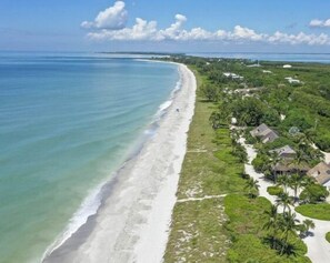 An aerial view of a beach with a clear shoreline, surrounded by lush greenery and small buildings.