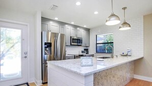A modern kitchen with white cabinetry, stainless steel appliances, a marble countertop, and pendant lighting. - South Seas Beach House 22 (Captiva)