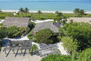 A coastal property with two buildings, a sandy beach, and palm trees.
