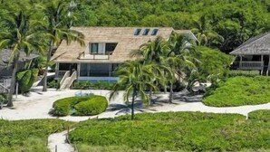 A beachfront property with a large house, palm trees, and a pathway leading to the beach. - South Seas Beach House 22 (Captiva)