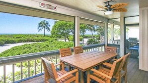 A covered outdoor dining area with a wooden table and chairs, overlooking a beach and lush greenery. - South Seas Beach House 22 (Captiva)