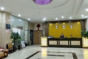 A hotel reception area with a receptionist, a reception desk, a clock, and a plant. - Danxia Holiday Hotel (Hezhou)
