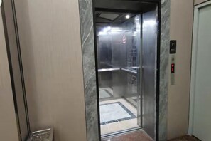 An elevator interior with a marble wall, a control panel with a red light, and a floor with a geometric pattern. - Danxia Holiday Hotel (Hezhou)