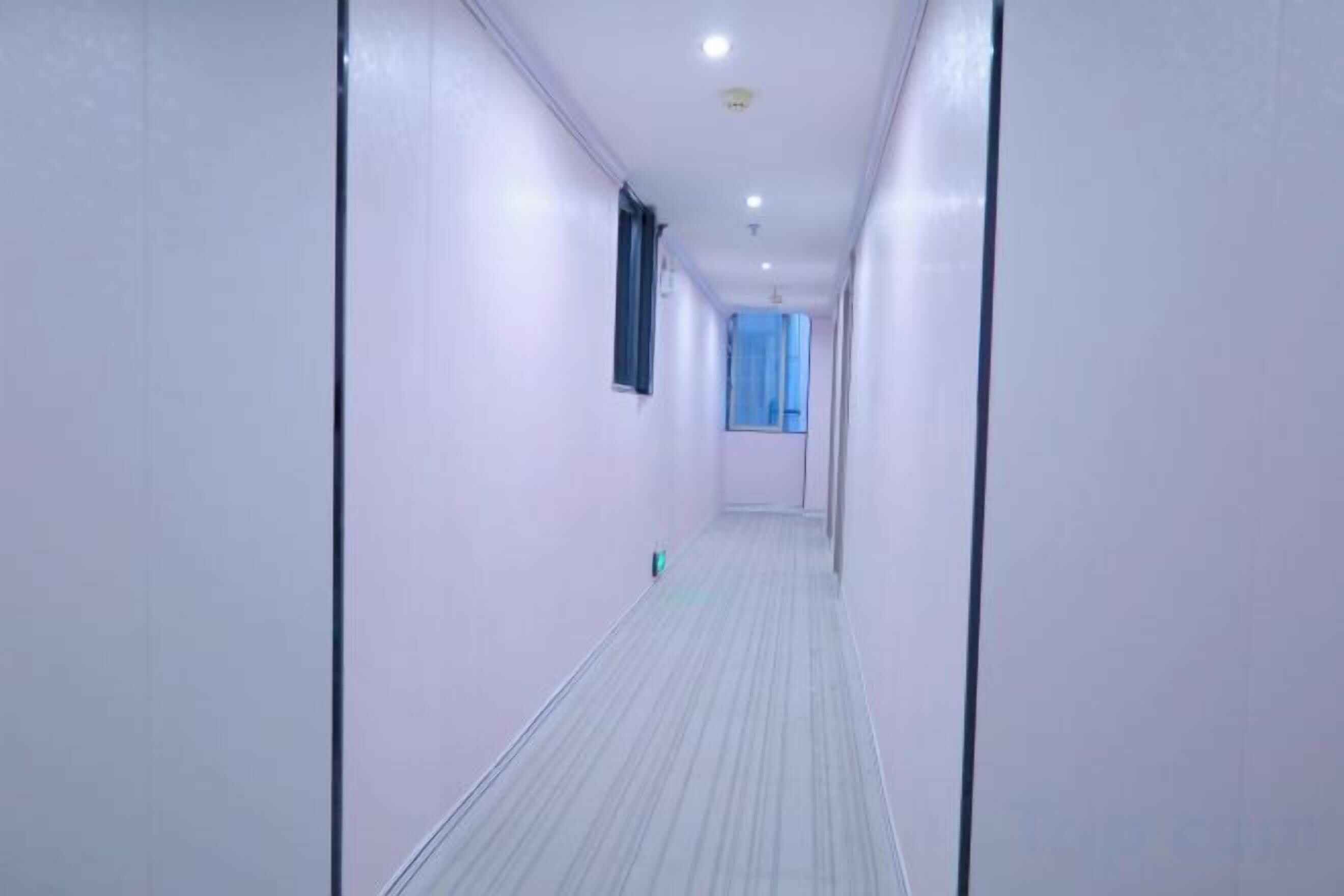 A narrow, well-lit hallway with a patterned floor and a window at the end.