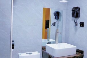 Un baño con un lavamanos blanco, un espejo y dos secadores de pelo fijados en la pared.