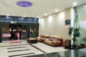 Un hall de hotel con mostrador de recepción, sofás de cuero, una mesa de centro y una planta en maceta.