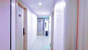 A hotel hallway with doors on both sides, a light-colored floor, and a ceiling light. - Danxia Holiday Hotel (Hezhou)