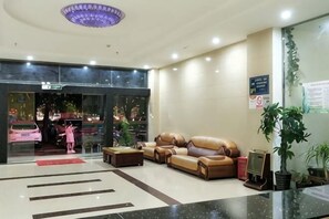 Un hall d’hôtel comprenant un comptoir d’accueil, des canapés en cuir, une table basse et une grande plante en pot.