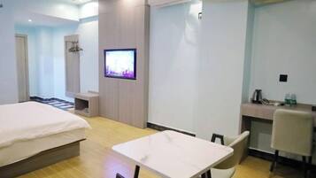 Quarto de hotel com cama, mesinha, televisão e escrivaninha com cadeiras.