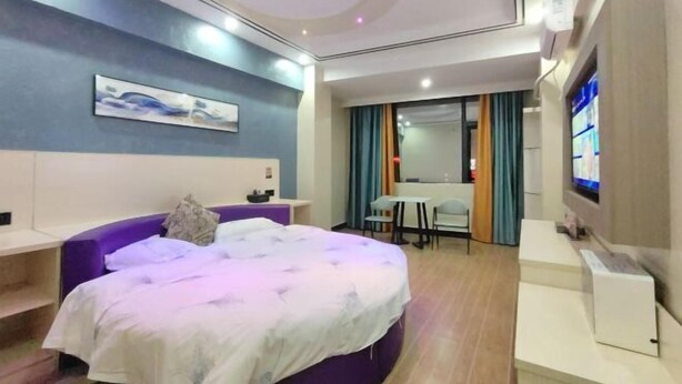 A modern hotel room with a bed, a desk, a TV, and a painting on the wall. - Danxia Holiday Hotel (Hezhou)
