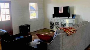 A living room with a high ceiling, a grey sofa, a television on a cabinet, and a wooden floor. - A beautiful Sunset Cottage. Amazing Mountain View’s and Sunsets. (Hendersonville)