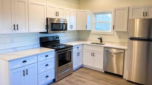 A modern kitchen with white cabinetry, stainless steel appliances, and a window providing natural light. - A beautiful Sunset Cottage. Amazing Mountain View’s and Sunsets. (Hendersonville)