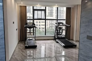 A room with a treadmill, a desk, and a large window with a city view. - Jilong Hotel (Longli County Traditional Chinese Medicine Hospital) (Longli)