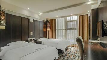 A hotel room with two beds, a desk, a chair, a TV, and a large window with curtains.