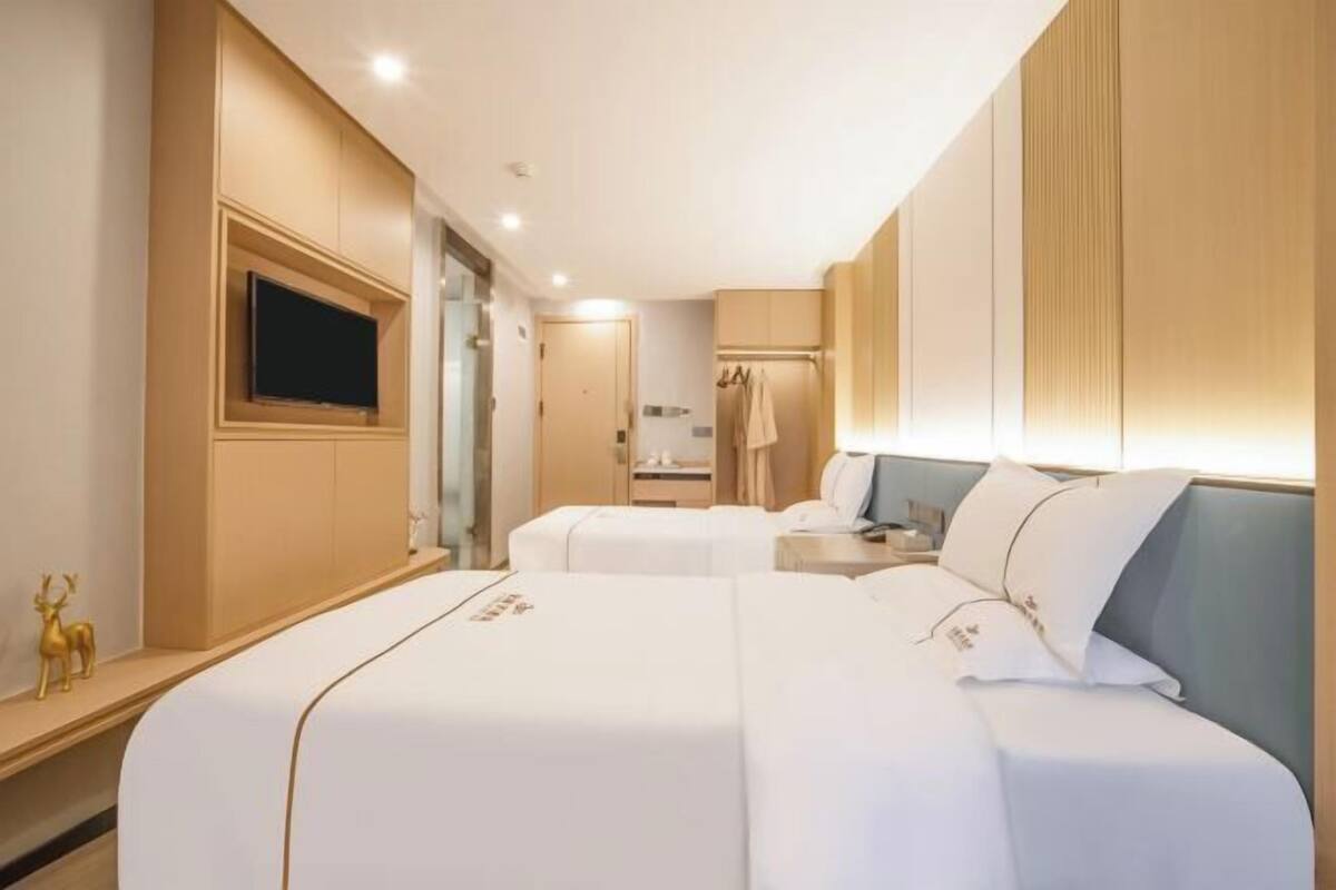 A hotel room with two beds, a TV, a minibar, and a bathroom.