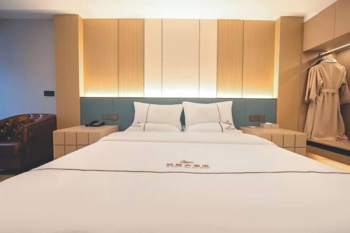 A hotel room with a large bed, bedside tables, a robe hanging on the wall, and a wooden headboard.