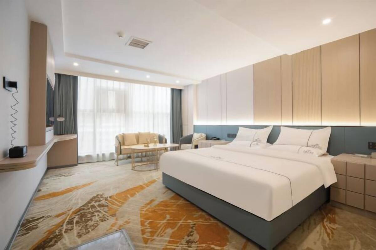 A modern hotel room with a large bed, a desk, a chair, and a view of the city.