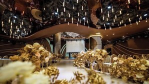 An interior with a central aisle decorated with golden foliage, a curved ceiling with hanging lights, and a stage area with a circular backdrop. - Jilong Hotel (Longli County Traditional Chinese Medicine Hospital) (Longli)