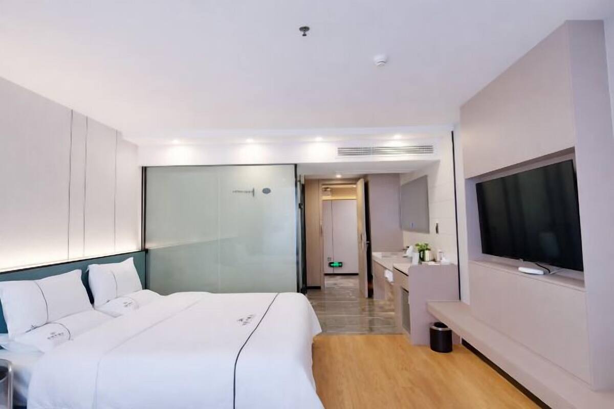 A modern hotel room with a bed, a TV, a desk, and a bathroom.