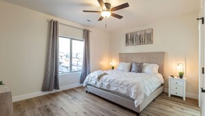Une chambre à coucher comprenant un lit, des tables de chevet, un ventilateur de plafond, une fenêtre avec des rideaux et une vue sur l’extérieur.
