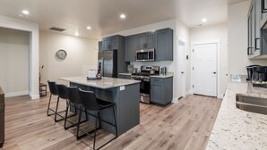 Une cuisine moderne avec des meubles gris, des appareils en acier inoxydable et un îlot central doté de tabourets de bar.