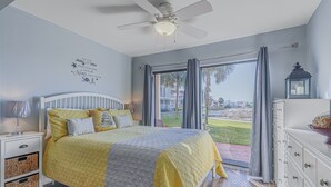 Un dormitorio con cama, mesita de noche, cómoda, ventilador de techo y vistas al exterior.