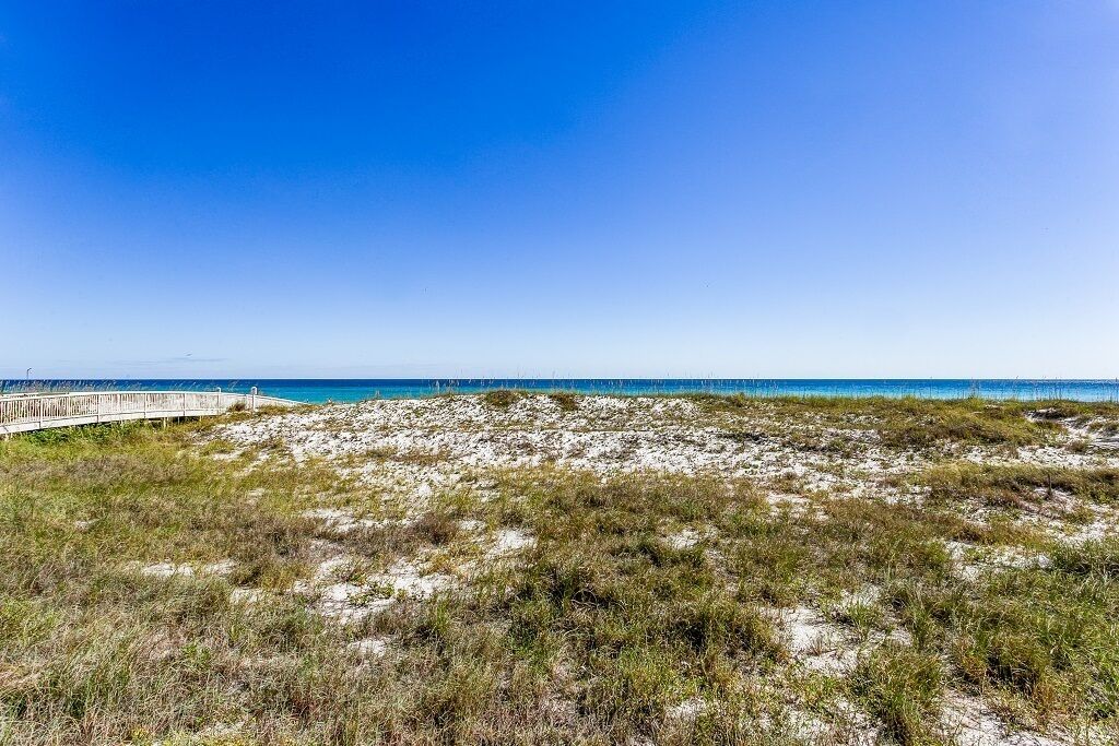 Une plage avec une promenade en bois qui mène à l’eau, des dunes de sable et un ciel bleu dégagé.